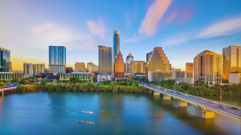 Austin skyline at sunset over Lady Bird Lake with a bridge and rowers